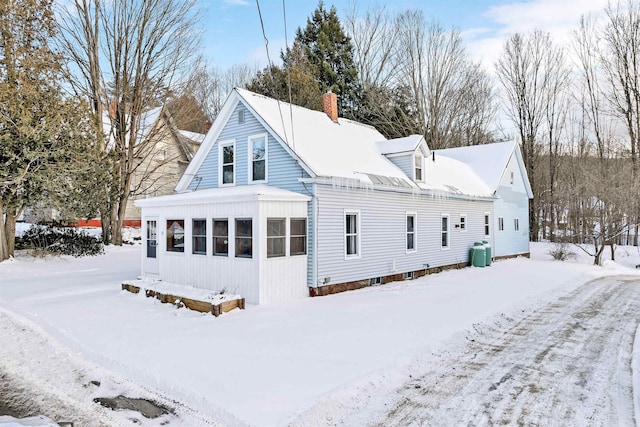 snow covered rear of property with a sunroom