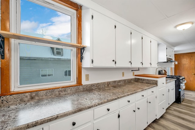 kitchen featuring black range with gas stovetop, light hardwood / wood-style floors, and white cabinets