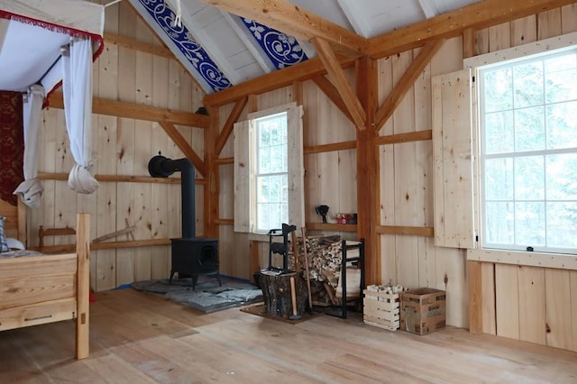 misc room with lofted ceiling, a wood stove, wood walls, and light wood-type flooring