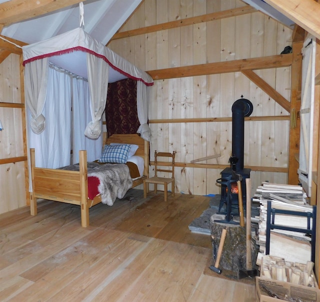 bedroom featuring wood-type flooring, vaulted ceiling, a wood stove, and wood walls