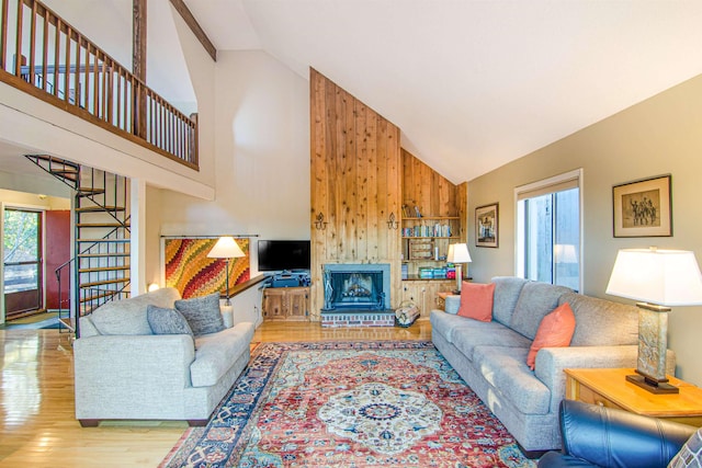 living room with wood-type flooring, high vaulted ceiling, wooden walls, and a fireplace