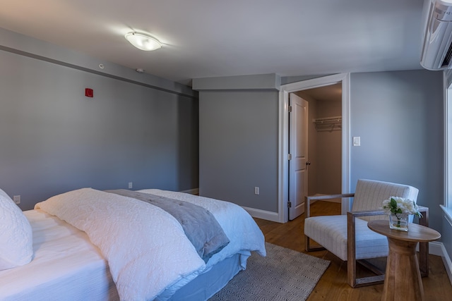 bedroom with a spacious closet, an AC wall unit, a closet, and hardwood / wood-style flooring