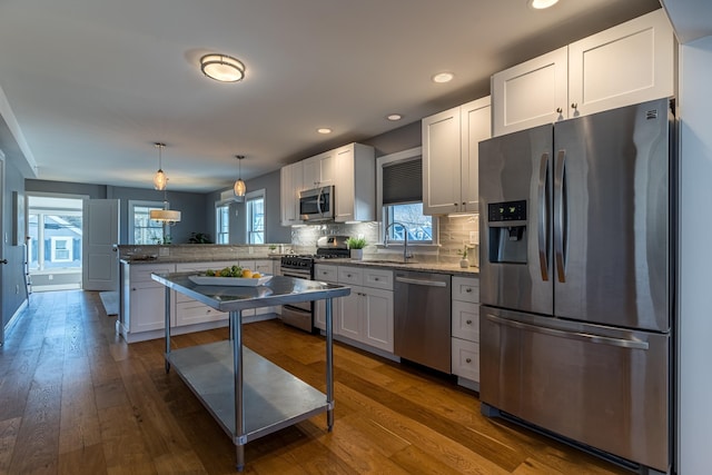 kitchen featuring hanging light fixtures, wood-type flooring, stainless steel appliances, and white cabinets