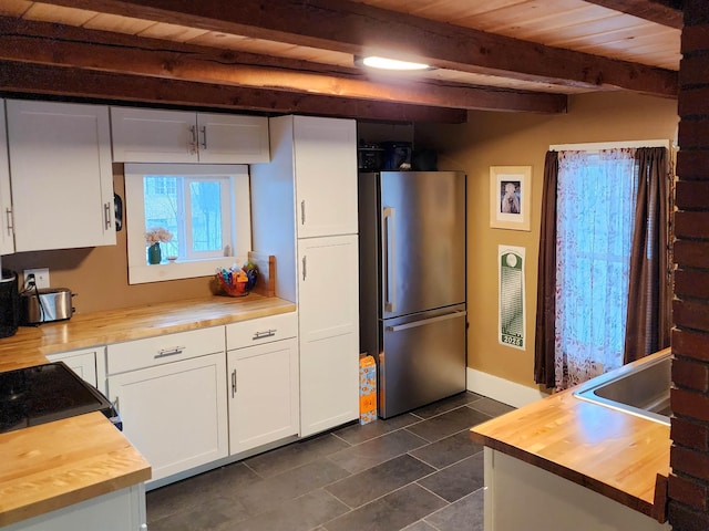 kitchen featuring butcher block counters, white cabinetry, wood ceiling, stainless steel refrigerator, and beamed ceiling