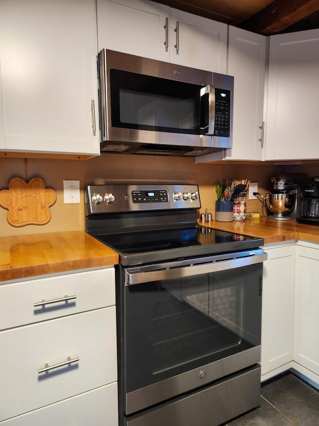 kitchen featuring appliances with stainless steel finishes, dark tile patterned flooring, butcher block countertops, and white cabinets