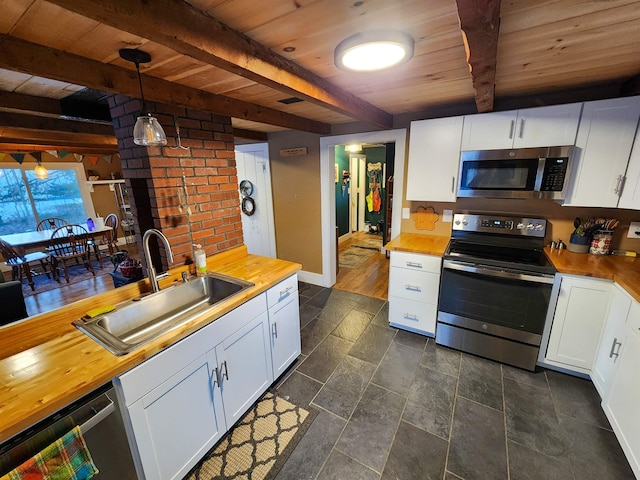 kitchen featuring appliances with stainless steel finishes, pendant lighting, white cabinetry, sink, and butcher block counters