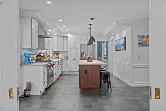 kitchen with a breakfast bar, high end stove, white cabinets, a kitchen island, and wall chimney exhaust hood