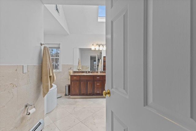 bathroom with vanity, a baseboard heating unit, tile walls, and a skylight