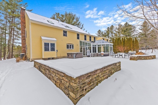 snow covered property with a lanai, central AC, and a hot tub