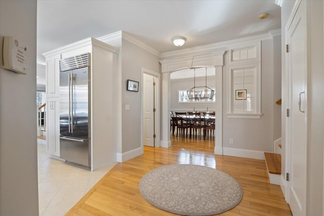 entryway with an inviting chandelier, light tile patterned floors, and crown molding