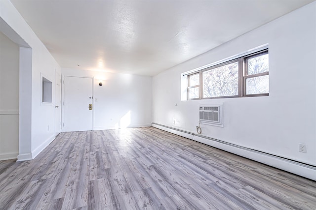 spare room featuring a baseboard heating unit, a wall mounted air conditioner, and light hardwood / wood-style floors