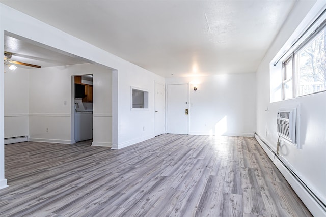 unfurnished living room featuring a baseboard radiator, washer / dryer, and light hardwood / wood-style floors