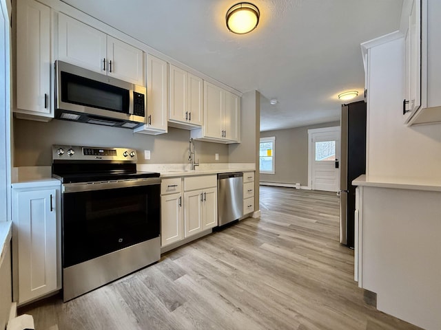 kitchen with stainless steel appliances, white cabinetry, sink, and light hardwood / wood-style flooring