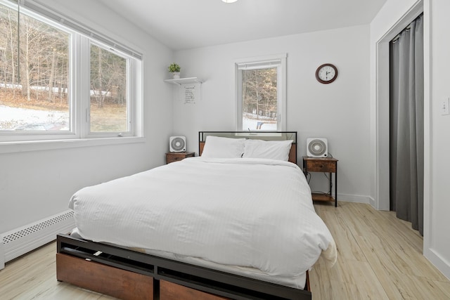 bedroom featuring a baseboard heating unit and light hardwood / wood-style floors