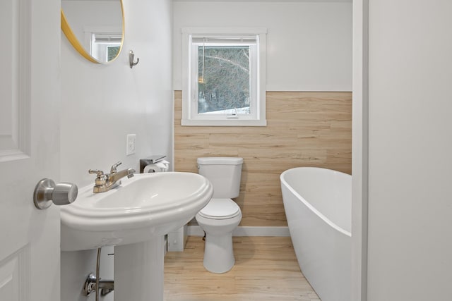 bathroom with a washtub, hardwood / wood-style floors, and toilet