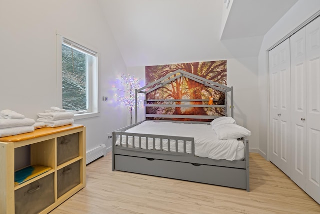 bedroom featuring baseboard heating, vaulted ceiling, light hardwood / wood-style floors, and a closet