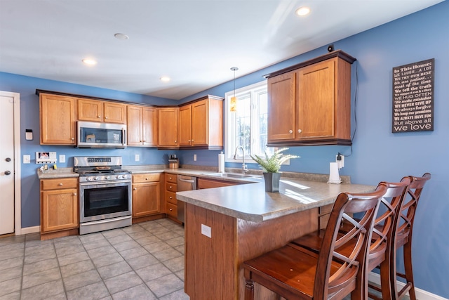 kitchen with a kitchen bar, sink, decorative light fixtures, appliances with stainless steel finishes, and kitchen peninsula