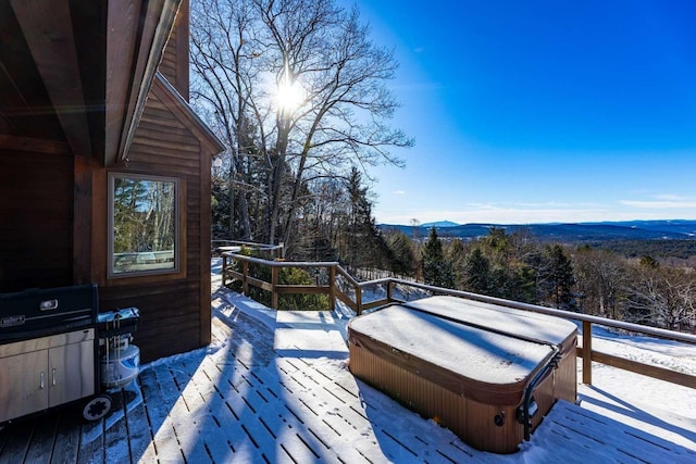 snow covered deck with a mountain view and a covered hot tub