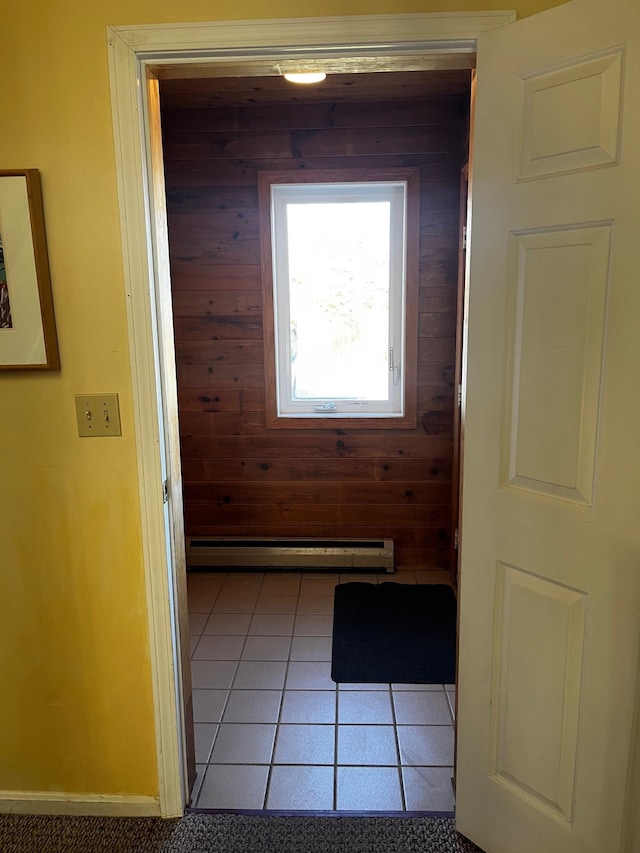 corridor with baseboard heating, wooden walls, and light tile patterned floors