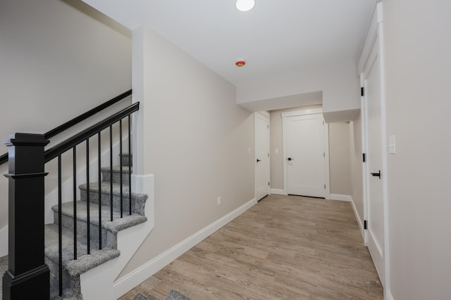 corridor with baseboards, stairs, and light wood-style floors