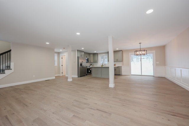 unfurnished living room with a wainscoted wall, recessed lighting, an inviting chandelier, light wood-type flooring, and stairs