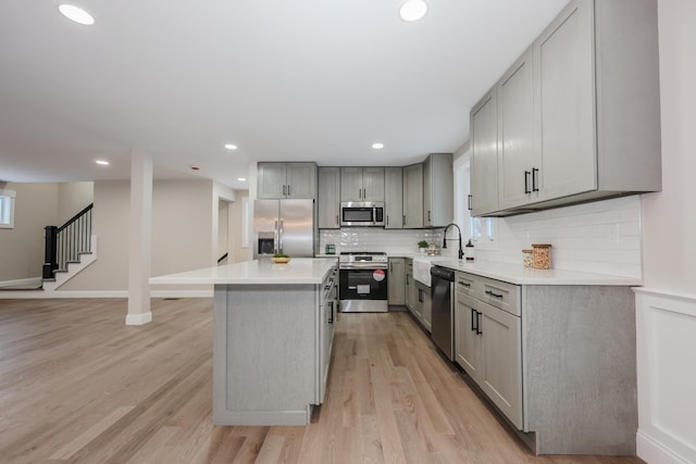 kitchen with gray cabinetry, appliances with stainless steel finishes, a kitchen island, light hardwood / wood-style floors, and backsplash