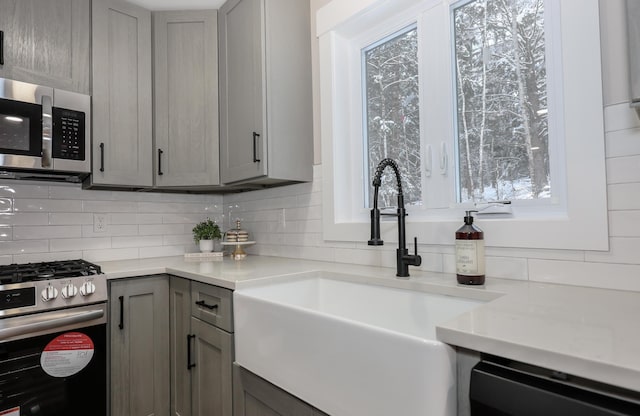 kitchen featuring a sink, appliances with stainless steel finishes, decorative backsplash, and gray cabinetry