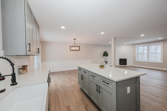 kitchen with gray cabinets, a kitchen island, pendant lighting, sink, and a large fireplace