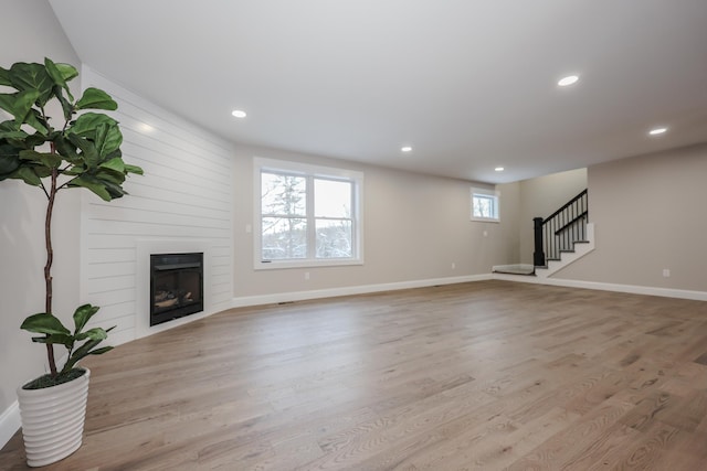 unfurnished living room with stairway, baseboards, recessed lighting, a large fireplace, and light wood-style floors