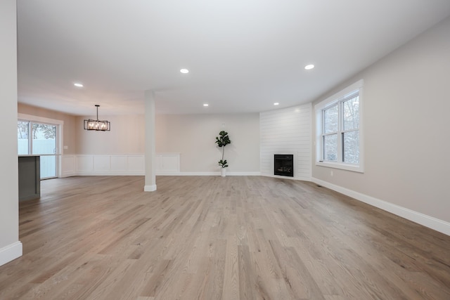 unfurnished living room with baseboards, an inviting chandelier, recessed lighting, a fireplace, and light wood-type flooring