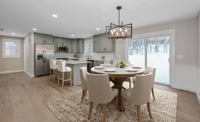 dining area with an inviting chandelier, sink, and light hardwood / wood-style flooring