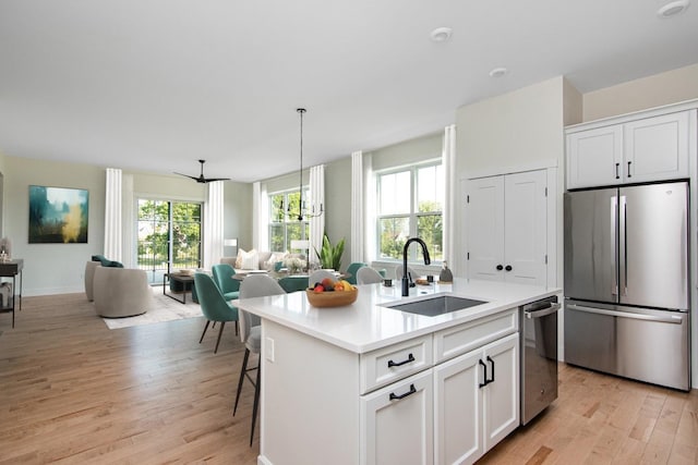 kitchen featuring sink, stainless steel appliances, an island with sink, white cabinets, and light wood-type flooring