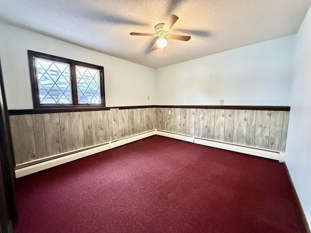 carpeted empty room with ceiling fan, a baseboard heating unit, a textured ceiling, and wood walls