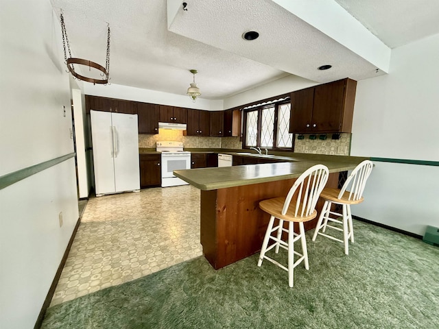 kitchen with white appliances, a breakfast bar, backsplash, dark brown cabinets, and kitchen peninsula