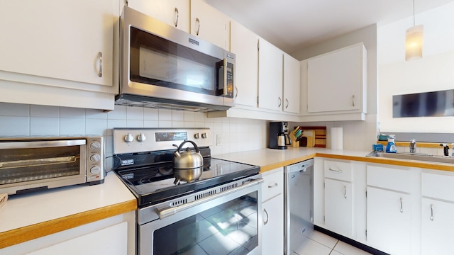 kitchen featuring sink, white cabinetry, hanging light fixtures, stainless steel appliances, and backsplash