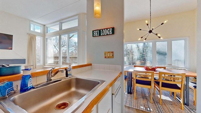 kitchen featuring dishwashing machine, sink, hanging light fixtures, a notable chandelier, and white cabinets