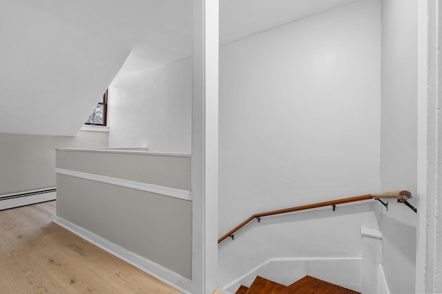 staircase with vaulted ceiling, a baseboard radiator, and hardwood / wood-style floors