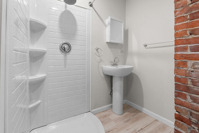 bathroom with a shower, brick wall, and wood-type flooring