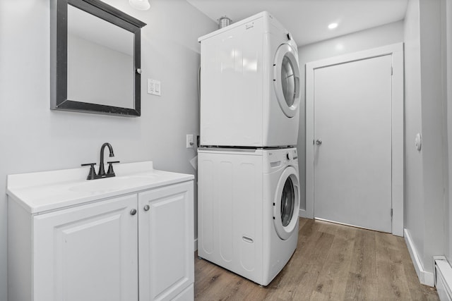 washroom with cabinets, stacked washer and clothes dryer, light hardwood / wood-style floors, and sink