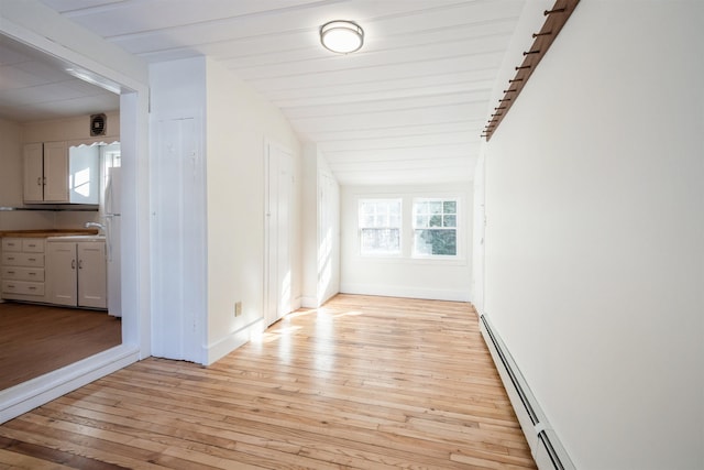 spare room featuring baseboard heating, lofted ceiling, sink, and light wood-type flooring