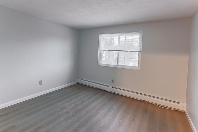 empty room featuring wood-type flooring, a baseboard heating unit, and a textured ceiling