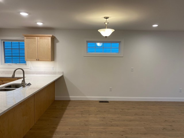 kitchen featuring light brown cabinetry, sink, light stone counters, hanging light fixtures, and dark hardwood / wood-style floors