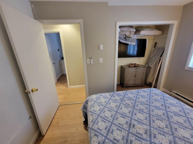 bedroom with a baseboard heating unit, a closet, and light wood-type flooring