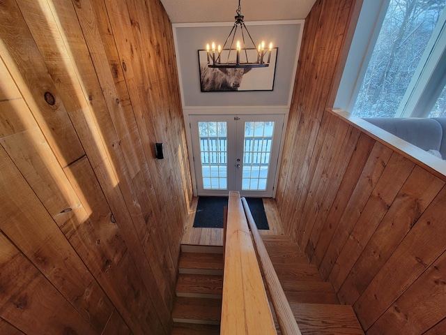 stairway with a notable chandelier, wood walls, and french doors