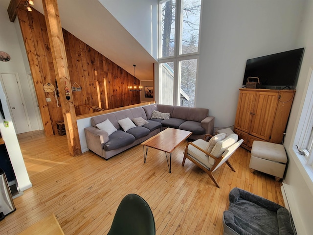 living room featuring wooden walls, a chandelier, high vaulted ceiling, and light hardwood / wood-style floors