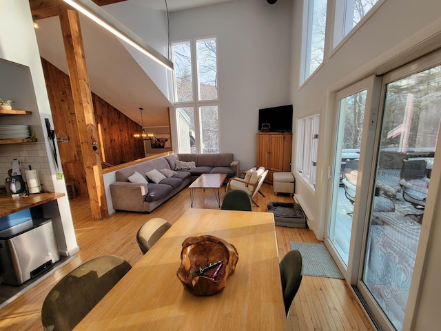 living room featuring a towering ceiling, wooden walls, light hardwood / wood-style flooring, and a notable chandelier