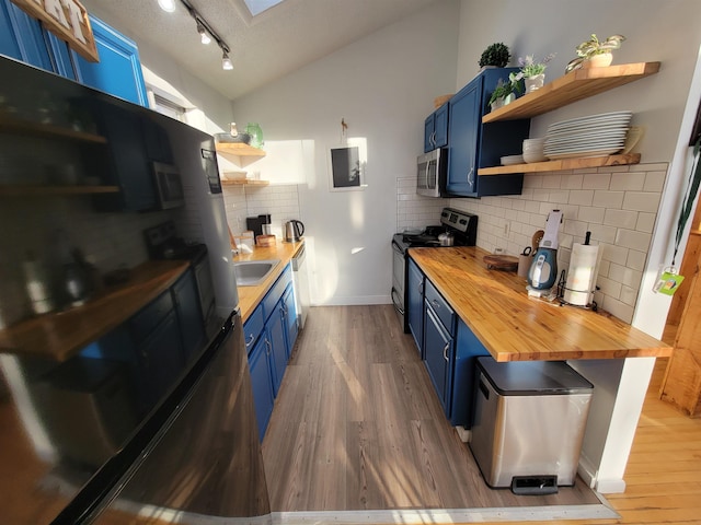 kitchen featuring lofted ceiling, blue cabinets, butcher block countertops, hardwood / wood-style flooring, and stainless steel appliances