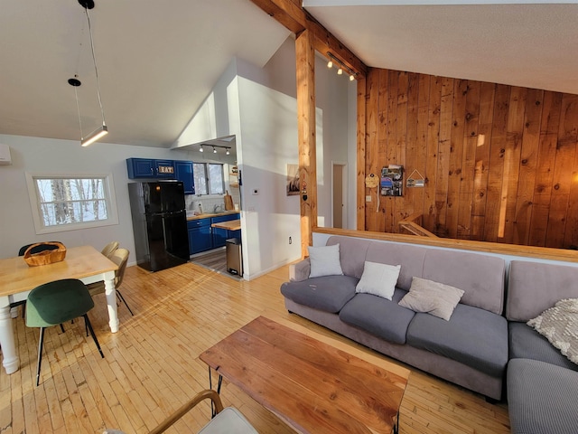 living room with light hardwood / wood-style flooring, vaulted ceiling with beams, and wooden walls