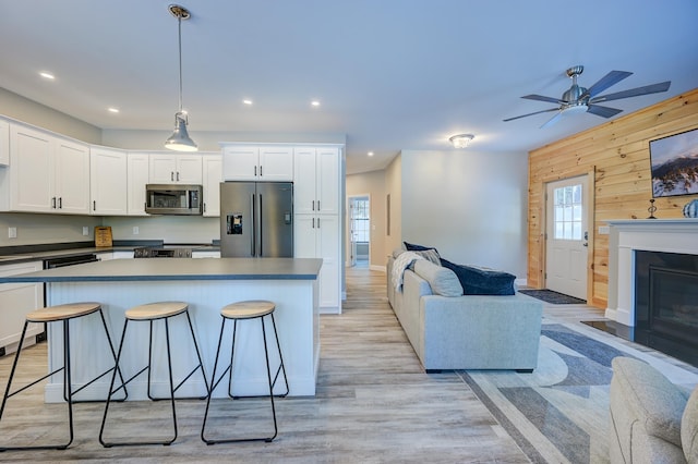 kitchen with white cabinetry, a kitchen breakfast bar, wooden walls, pendant lighting, and stainless steel appliances