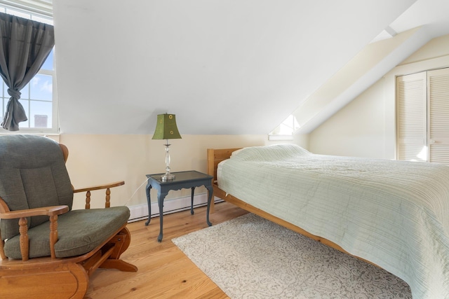 bedroom with lofted ceiling with skylight, light wood-type flooring, and a baseboard heating unit